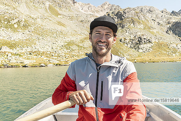 Young smiling man in a rowing boat  Lake Suretta  Graubuenden  Switzerland