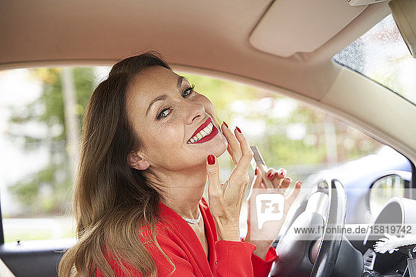 Porträt einer glücklichen reifen Frau mit roten Lippen und Nägeln im Auto