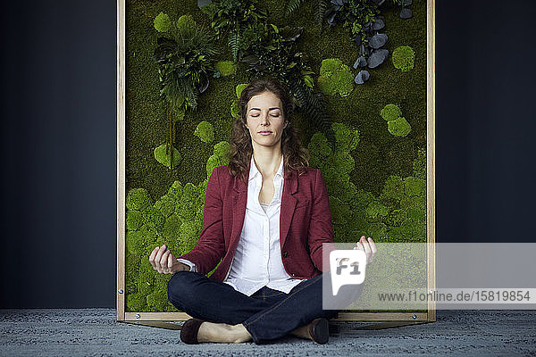 Businesswoman sitting on the floor in green office practicing yoga