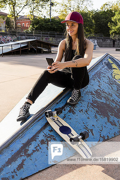 Junge Frau mit Smartphone und Skateboard im Skatepark