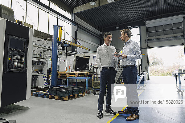 Zwei Männer mit Tablette im Gespräch in einer Fabrik