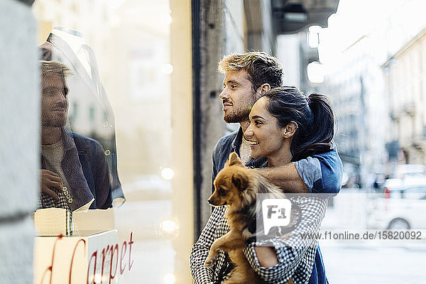 Junges Paar mit Hund schaut in ein Schaufenster in der Stadt