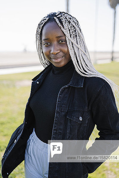 Porträt einer lächelnden Teenagerin mit Zöpfen im Freien