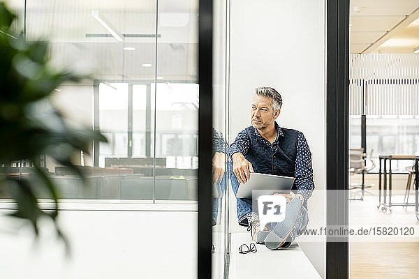 casual businessman sitting on windowsill in office building  using laptp