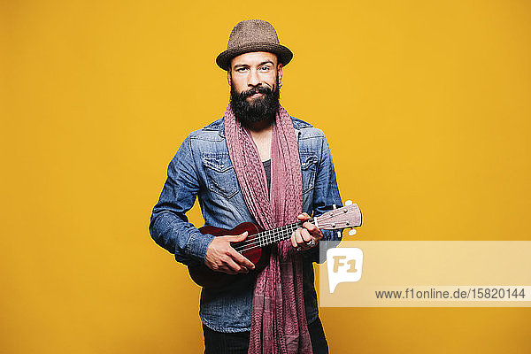Porträt eines bärtigen jungen Mannes im Atelier mit Ukulele