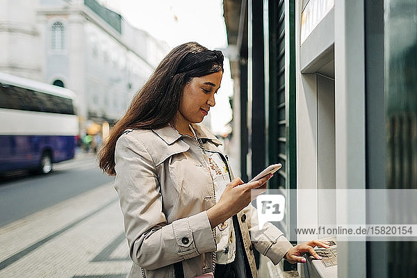 Frau benutzt Geldautomat und Mobiltelefon