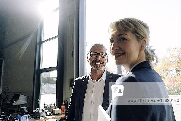 Porträt eines lächelnden Geschäftsmannes und einer lächelnden Geschäftsfrau am Fenster in einer Fabrik