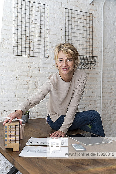 Portrait of smiling mature woman sitting on desk in architectural office