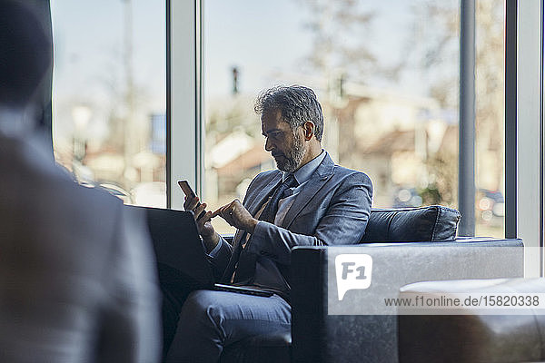 Geschäftsmann benutzt Laptop und Smartphone in der Hotellobby