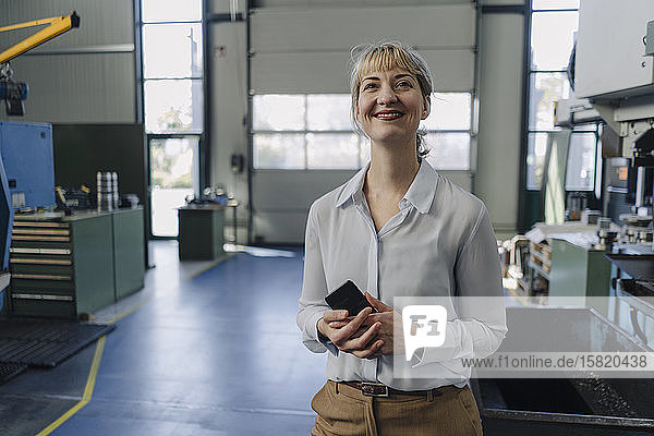 Porträt einer lächelnden Geschäftsfrau mit Handy in einer Fabrik