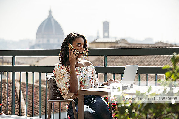 Junge Frau benutzt Laptop und telefoniert auf einem Balkon in Florenz  Italien