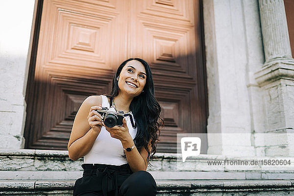 Porträt einer glücklichen jungen Frau  die auf einer Treppe sitzt und mit der Kamera fotografiert  Lissabon  Portugal