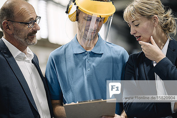 Geschäftsleute und Arbeiter mit Zwischenablage im Gespräch in einer Fabrik