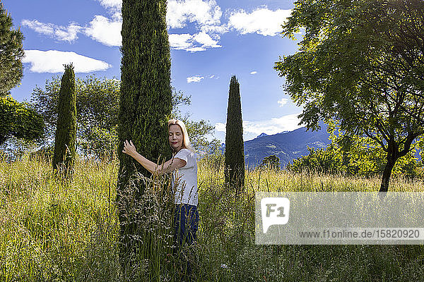 Woman standing in meadow hugging cypresse