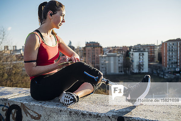 Sporty young woman with leg prosthesis sitting on a wall above the city  Milan  Italy