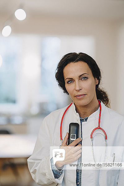 Female doctoe standing in hosptal  holding telephone and stethoscope