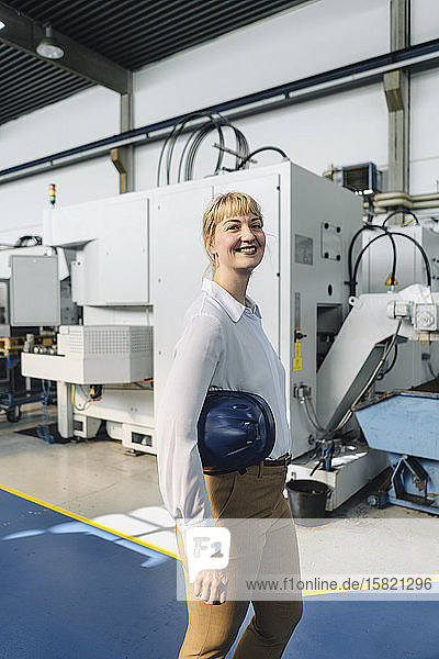 Porträt einer lächelnden Geschäftsfrau mit Schutzhelm in einer Fabrik