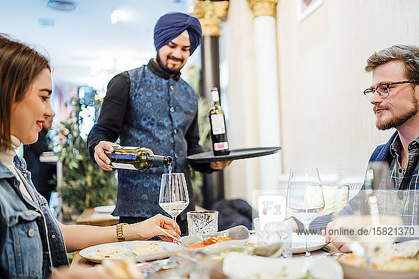 Freunde essen in einem indischen Restaurant  Kellner gießt Wein in Gläser