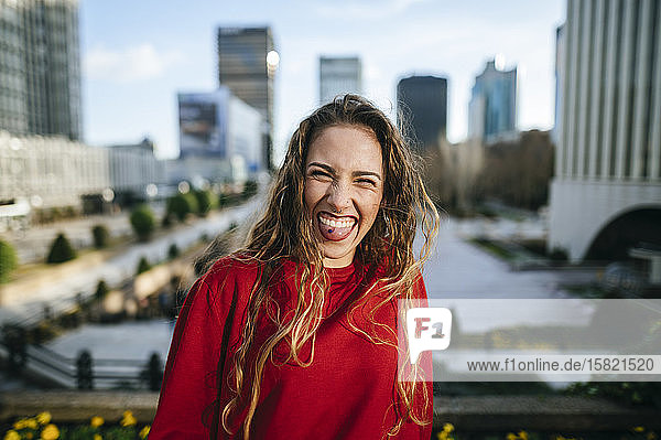 Porträt einer glücklichen jungen Frau in der Stadt  die ihre Zunge herausstreckt