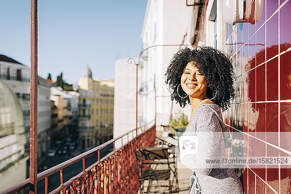 Porträt einer glücklichen jungen Frau mit lockigem Haar auf dem Balkon