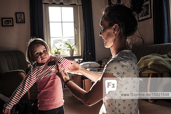 Mother dressing her little daughter in the living room