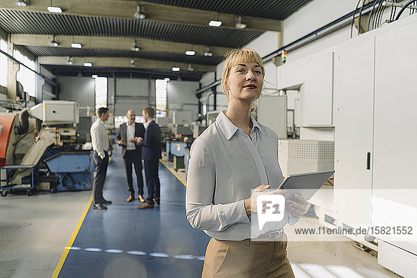 Porträt einer selbstbewussten Geschäftsfrau mit Tablette in einer Fabrik mit Kollegen im Hintergrund