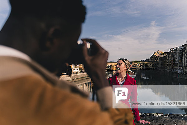 Junger Mann fotografiert seine Freundin auf einer Brücke über dem Arno  Florenz  Italien