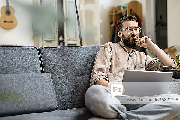Junger Mann sitzt zu Hause auf dem Sofa und benutzt ein digitales Tablett