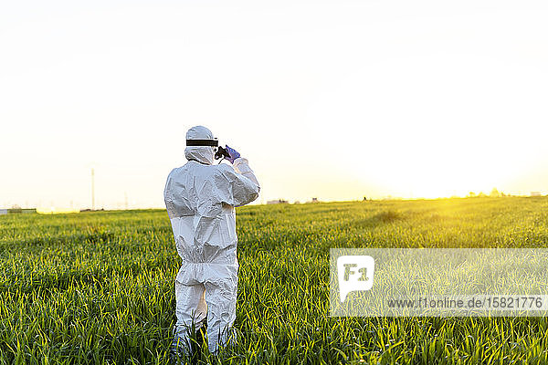Female scientist researching in field and looking through binoculars at sunset