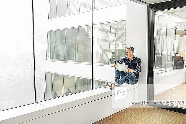 Casual businessman sitting on windowsill in office building  using laptp