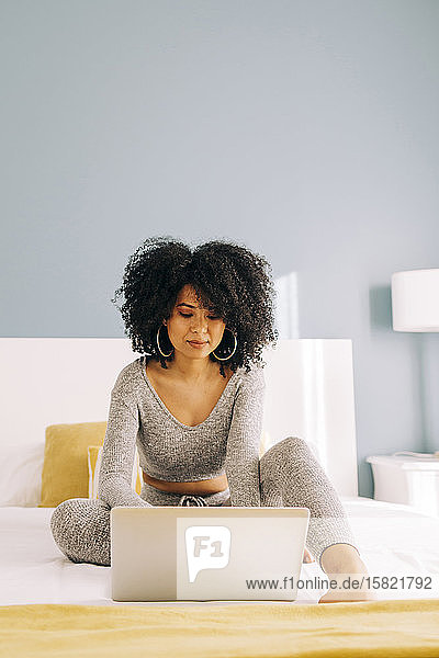 Porträt einer jungen Frau mit lockigem Haar mit Laptop auf dem Bett zu Hause