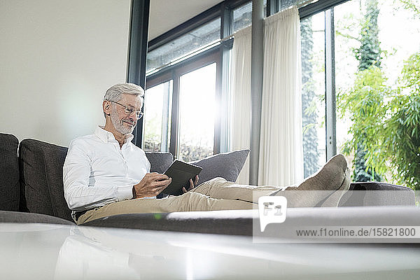Älterer Mann mit grauen Haaren in modernem Design-Wohnzimmer auf Couch sitzend mit Tablett