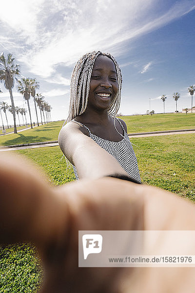 Porträt einer glücklichen Teenagerin mit Zöpfen  die ihre Hand im Freien ausstreckt
