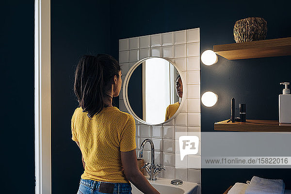 Young woman looking in bathroom mirror