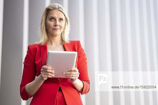 Blonde Geschäftsfrau in rotem Anzug und mit digitalem Tablet