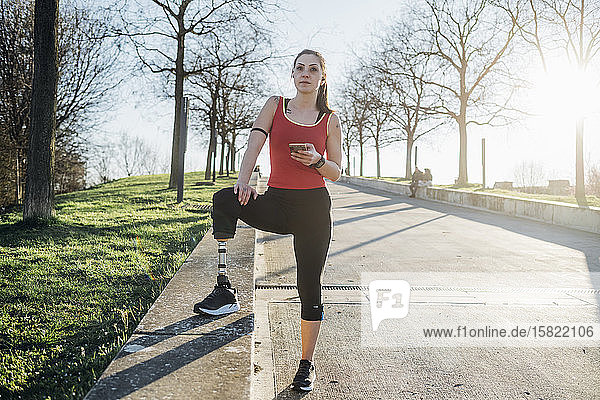 Sportliche junge Frau mit Beinprothese  die ein Mobiltelefon hält