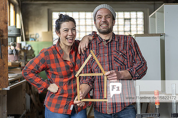 Porträt einer glücklichen Handwerkerin und eines Handwerkers  die in ihrer Werkstatt Messlatte halten