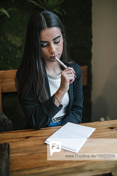 Porträt einer nachdenklichen jungen Frau in einem Café  die sich Notizen macht