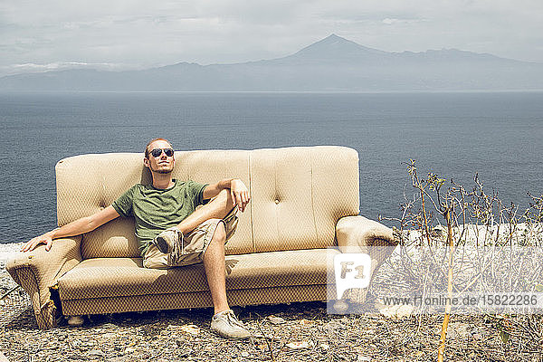 Junger Mann entspannt sich auf kaputter Couch und genießt die Sonne  La Gomera  Spanien