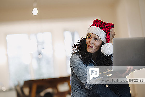 Woman with Santa hat looking for presents online  using laptop