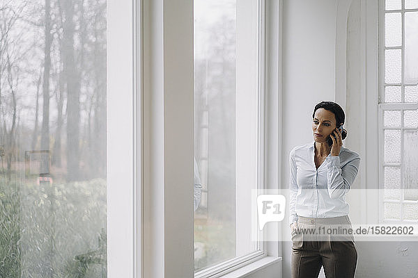 Erfolgreiche Geschäftsfrau  steht am Fenster und telefoniert