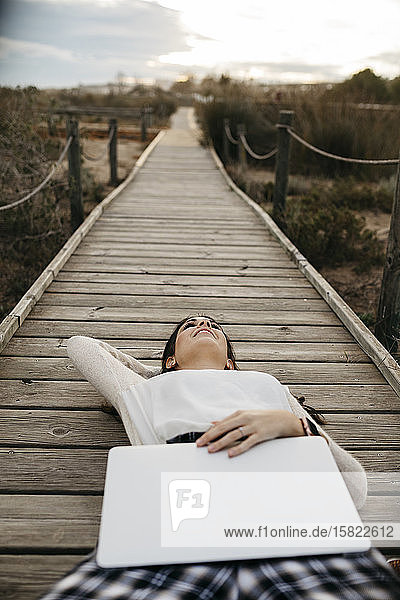 Woman lying on a boardwalk in the countryside with laptop