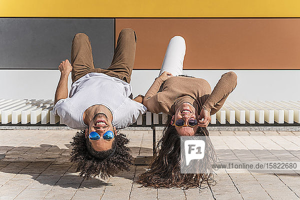 Paar mit Sonnenbrille  auf der Bank entspannen  auf dem Rücken liegend  Köpfe herunterhängen