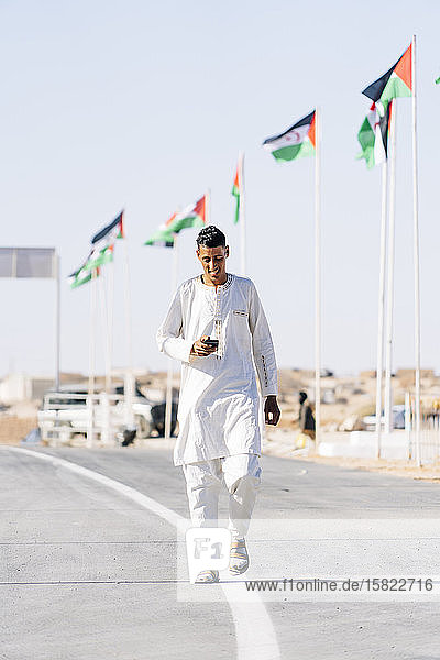 Mann benutzt Mobiltelefon beim Gehen auf der Straße im Flüchtlingslager Smara  Algerien