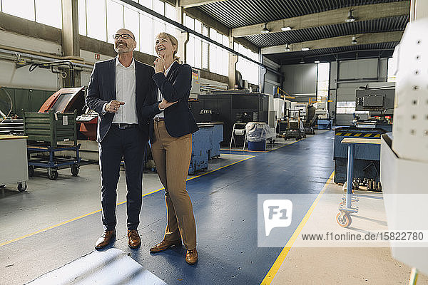 Confident businessman and businesswoman in a factory looking up