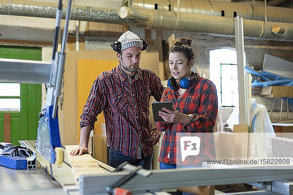 Handwerkerin und Handwerker mit Tablette diskutieren in ihrer Werkstatt