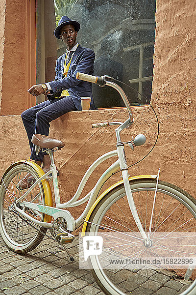 Stilvoller junger Geschäftsmann mit Fahrrad in altmodischem Anzug auf einem Fensterbrett sitzend
