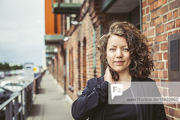 Porträt einer lächelnden brünetten Frau vor einem Backsteingebäude