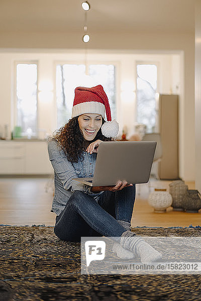 Frau mit Weihnachtsmannmütze sucht online nach Geschenken  mit Laptop