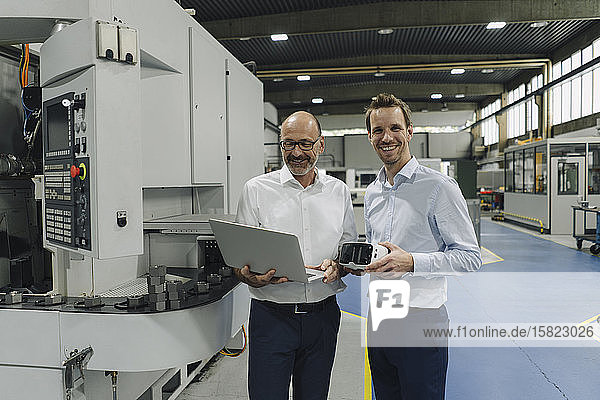 Portrait of two smiling men in a factory with laptop and VR glasses